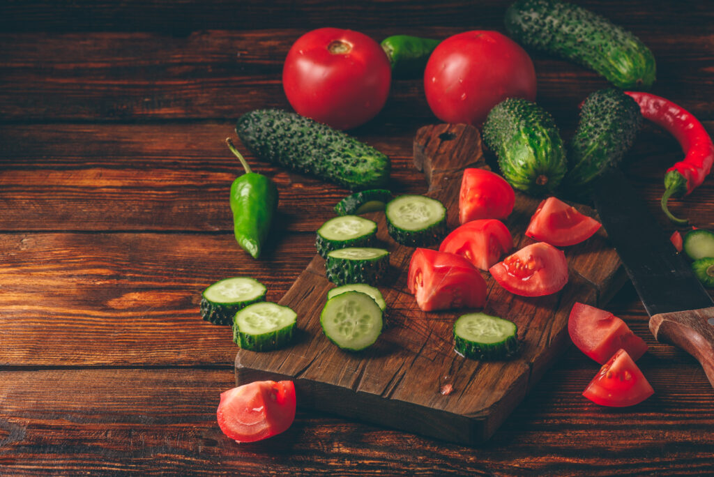 Sliced vegetables. Tomatoes, cucumbers and chili peppers over wooden background.